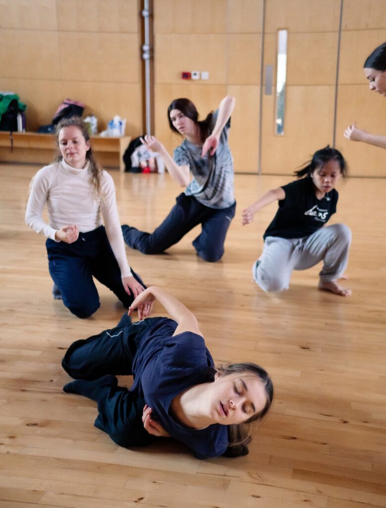 An image of four dancers dancing on the floor in a studio.