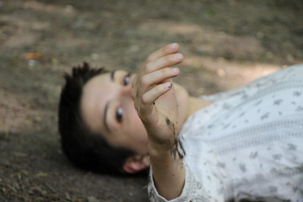 A dancer lying the the ground, their hand held up in front of the face.