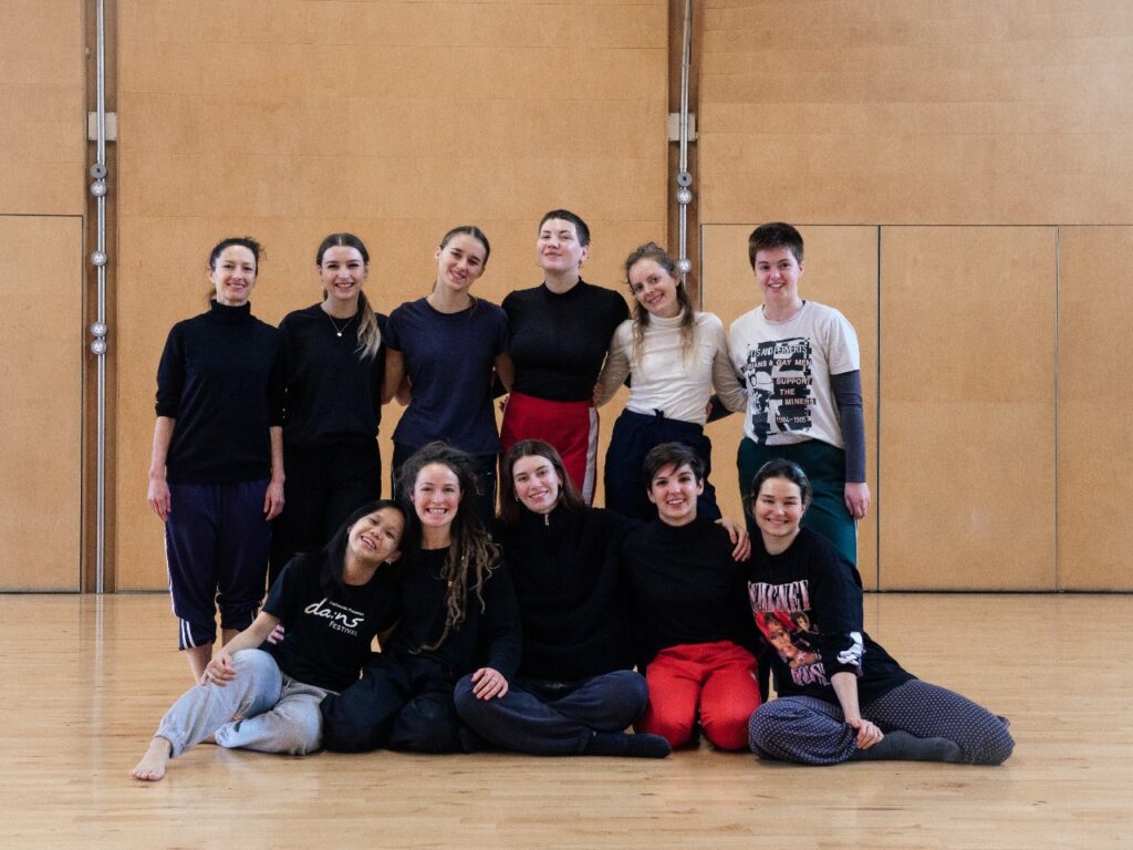 Dancers from the first edition of the Burgeon posing, smiling in a dance studio.