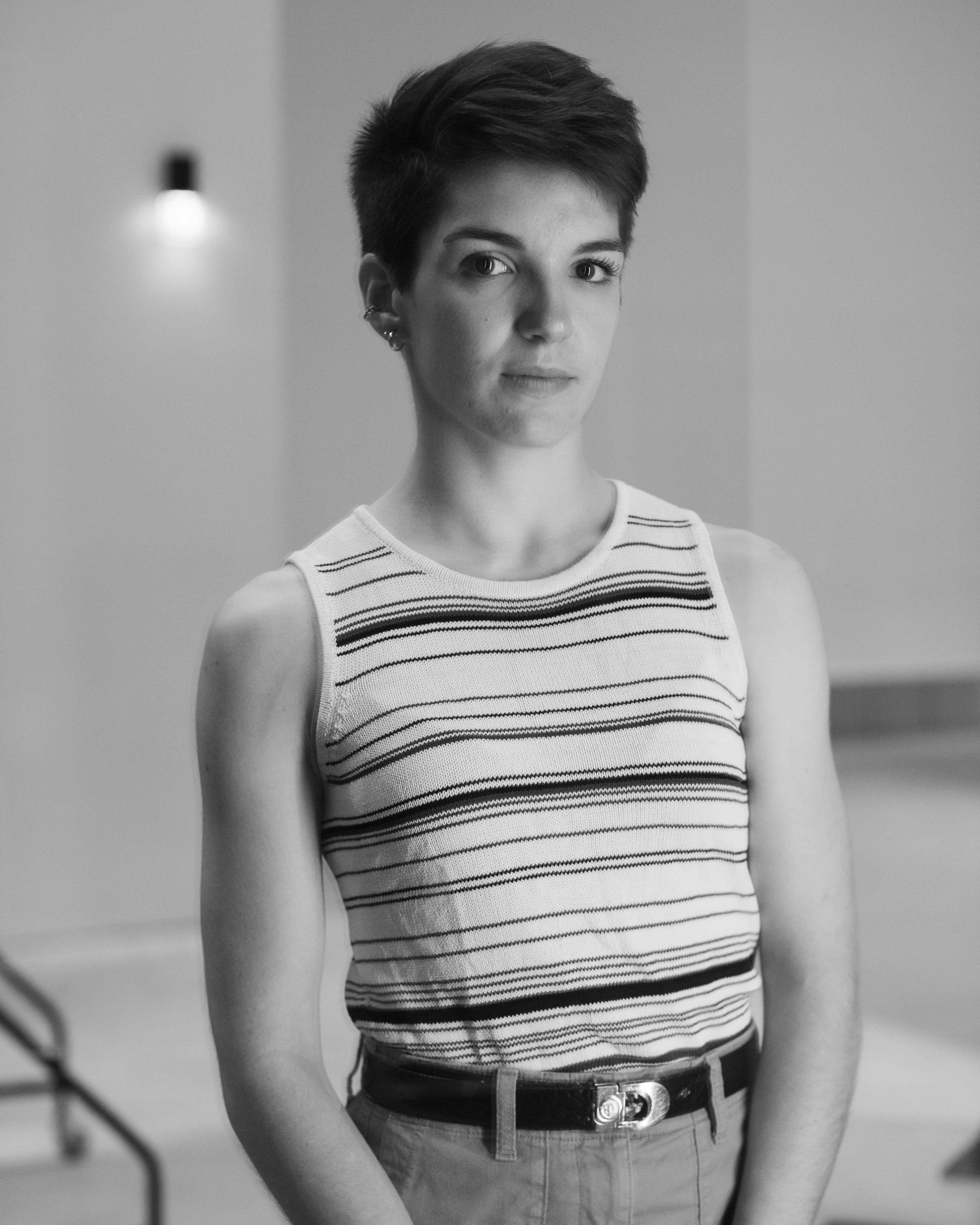 Black and White headshot of Laure. Laure is standing in an empty room looking directly at the camera, slightly smiling.